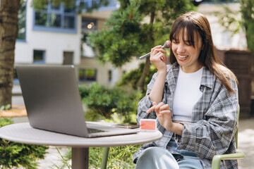 Woman learning makeup tutorial outdoors with laptop