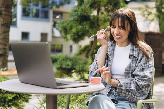 Woman learning makeup tutorial outdoors with laptop