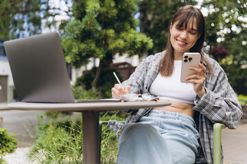 Woman remote working outdoors using laptop and smartphone