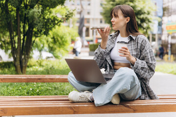 Woman sending voice message working on laptop in park