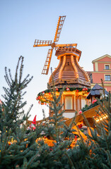 Vertical winter scene featuring a bright Christmas windmill surrounded by holiday decorations. Ideal for festive campaigns, tourism materials, market visuals, and seasonal advertising.