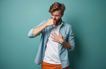Young European man coughs into fist. Grimaces in pain, discomfort. One hand grips chest tightly. Guy feels sick unwell from flu cold virus. Respiratory problem allergy asthma symptom. Sickness