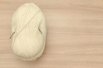 Beige yarn with knitting needles lies on a wooden table. Space for text.