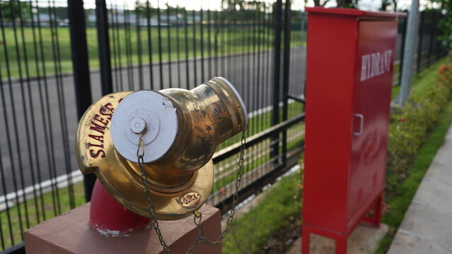 Gold-colored brass Siamese connection for fire hydrant system. Close-up of fire department connection (FDC) used for emergency water supply, firefighting operations, and building safety infrastructure