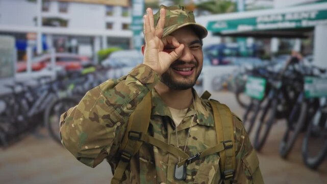 Man in camouflage uniform with dog tags makes ok sign next to rows of bike rental stands on street; approval.