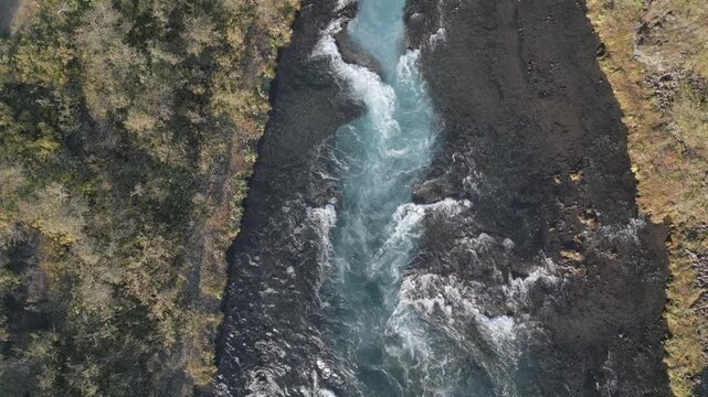 Dynamic aerial view of rushing river cutting through Iceland's stark landscape, powerful nature