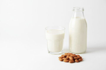 Almond milk in a clear glass next to a bottle, with scattered almonds on a white background, showcasing a healthy dairy alternative for nutrition and wellness