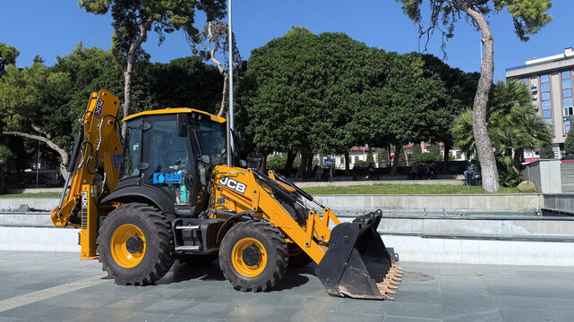 Antalya, Turkey - October 16, 2025: JCB backhoe loader parked in urban park with trees and greenery