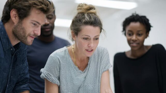three colleagues gathered around laptop, surprised and smiling as they review prototype in modern open-plan office; product designer points at screen