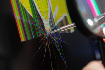 Technician uses screwdriver and magnifying glass to examine a severely cracked electronic display...