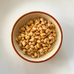 Lightly roasted pine nuts in a small ramekin on a white background, close-up, healthy snack.