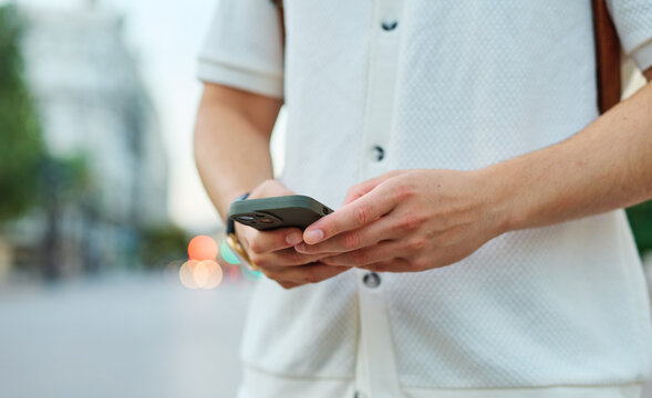 Young man enjoys sunny day while using smartphone in urban setting, highlighting his joy and connection to the world around him