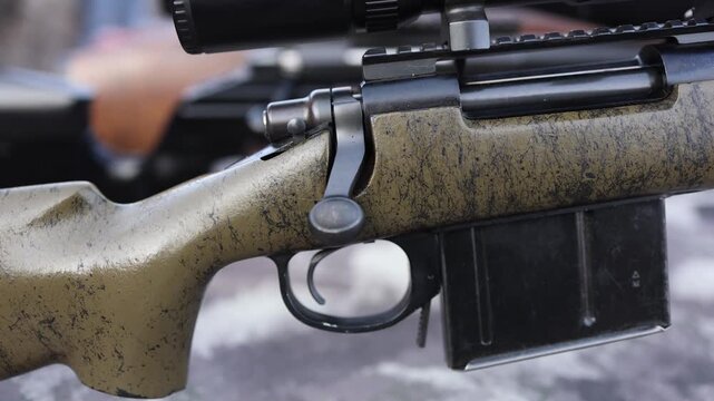 Close view of a bolt action rifle with textured stock focusing on the metal bolt handle and trigger area creating a technical atmosphere of precision mechanics and outdoor shooting equipment on a rang