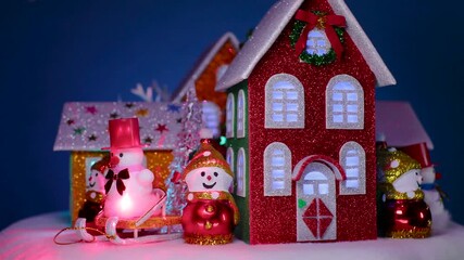 On a dark blue background, a Christmas village with colorful houses, snowmen, and Christmas trees next to them is rotating