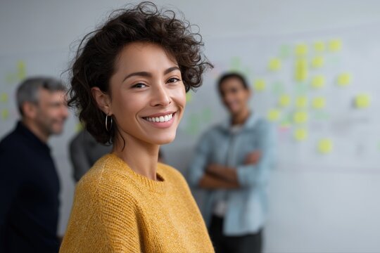 Confident hispanic young woman smiling in office with colleagues in background