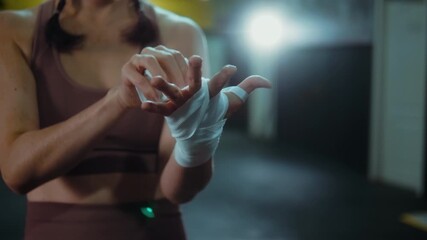 Close-up of a woman wrapping her hand with bandages, focused and precise as she prepares for an intense boxing training session in a gym. - Powered by Adobe