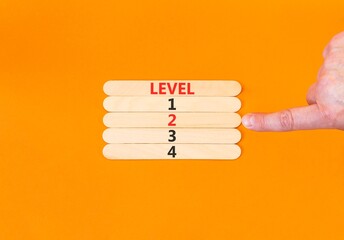 Time to level 2 symbol. Concept word Level 1 2 3 4 on beautiful wooden sticks. Businessman's hand. Beautiful orange background. Business planning and time to level 2 concept. Copy space.