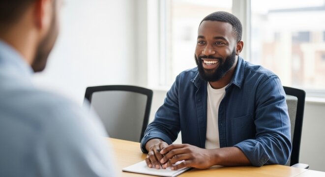 A friendly and confident young professional man with a beard smiling happily while listening during a business meeting or job interview in a modern, sunlit office