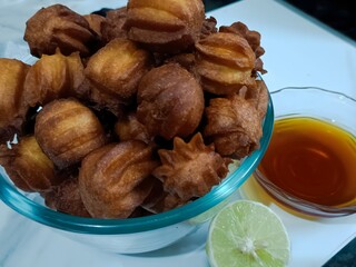 A bowl of crisp golden fritters served with honey and fresh lemon. The close-up shot highlights their texture, making this sweet snack look warm and appetizing.
