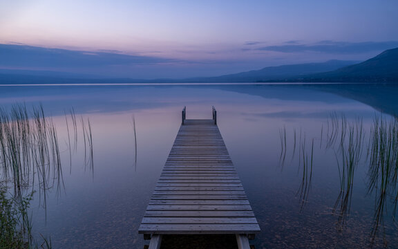 Wooden pier extending into a calm lake at twilight with purple sky and distant mountains