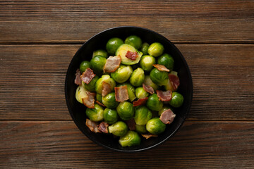 Top view of Brussels sprouts roasted with bacon in bowl wooden surface