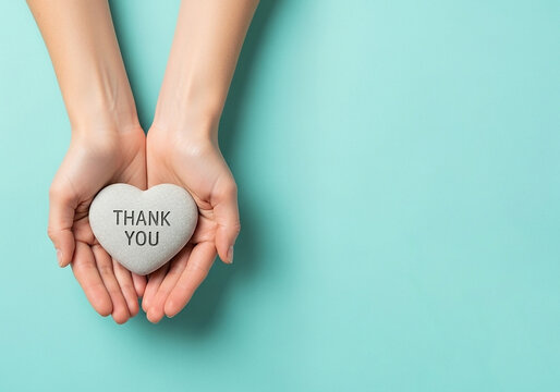 Top-down view of hands presenting a heart-shaped stone with 'Thank You', a minimalist and peaceful image perfect for conveying heartfelt appreciation