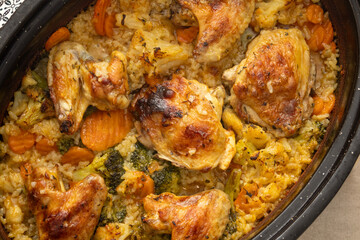 A baked chicken and vegetable rice dish in a black pot photographed from above, showing colorful ingredients, golden roasted texture, and the comforting warmth of a freshly prepared homemade meal.