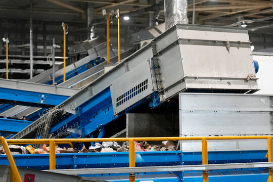 Conveyor belts at a waste sorting facility are moving mixed materials for efficient recycling. Workers oversee the operation to ensure proper sorting and processing of waste materials