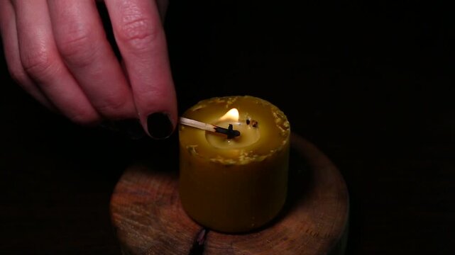 Woman hand lights a match the bees wax candle on wooden candlestick for mood, relaxation, meditation dark black background. Person lighting the decoration handmade one candle flame