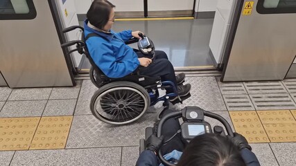 Two individuals in wheelchairs navigate train platform gap, showcasing accessibility features, camera pans and zooms to capture movement and interaction