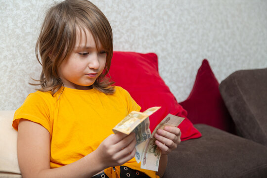 Little girl counting cash russian rubles money on the sofa at home