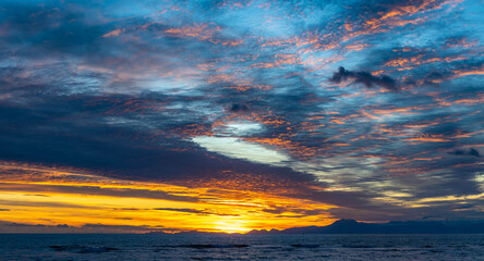 Fototapeta premium A picturesque sunset over the Mediterranean Sea in Side, with golden-lit clouds against a blue sky and dark blue waters. A stunning evening scene in Antalya, Turkey.