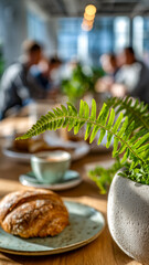 Warm cafe scene with a croissant, coffee, and a fern in soft lighting, creating an inviting and cozy atmosphere for socializing. 