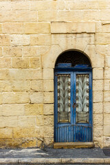 Blue Arched Window With Intricate Iron Grille Set in Cream Stone Wall Facade