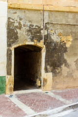 Weathered City Wall With Arched Doorway Leading to Dark Tunnel on Worn Facade