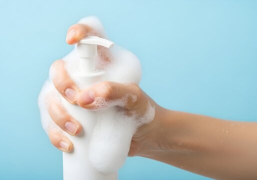 Hand pumping foamy soap from white dispenser against clean blue background, showing hygiene and handwashing concept