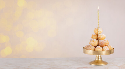 Cream puff tower dusted with powdered sugar on a golden stand with a lit festive candle