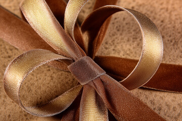 Elegant brown and gold ribbon bow for festive gift wrapping on textured background