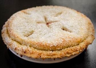 A perfectly baked cherry pie, featuring a golden, flaky crust generously coated with large sugar crystals, resting on a white plate after cooling.