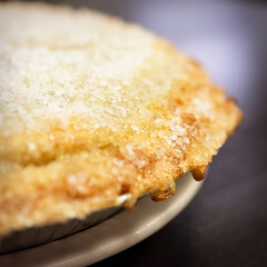 A dramatic close-up of the baked cherry pie's crust, showing the texture of the golden pastry and the thick, sparkling sugar topping in the cafe.