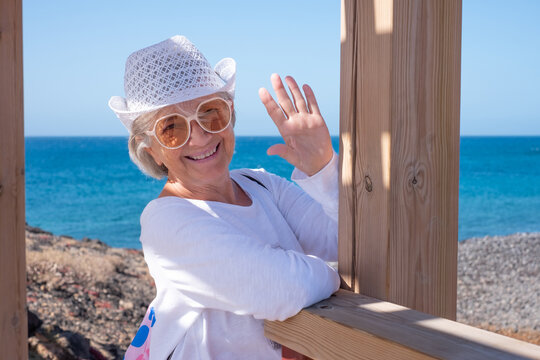 Happy senior tourist woman enjoying a sunny day relaxing at the seaside looking at camera, with the ocean and rocky coastline in the background