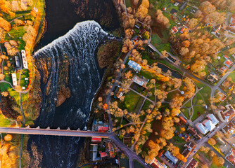 Aerial top down view of small European town with river waterfall, bridge, autumn trees and colorful houses on a sunny evening, scenic urban landscape background
