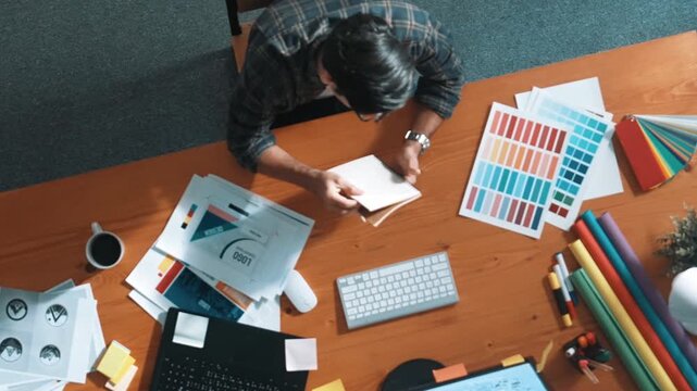 Top view of smart businessman hand choosing color palettes while designing logo graphic. Aerial view of professional interior designer design and select color theme by using color palettes. Symposium.