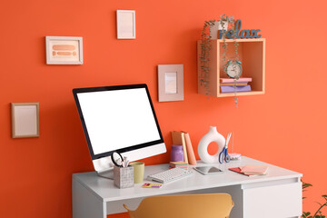 Inventor's workplace with blank computer near orange wall in office interior