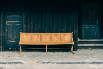 A long wooden bench stands against a dark weathered wall, creating a striking contrast between warm...
