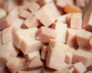 A close-up, high-angle view of a large pile of freshly cubed, pink, savory ham pieces, ready to be used as an ingredient in a cafe kitchen.