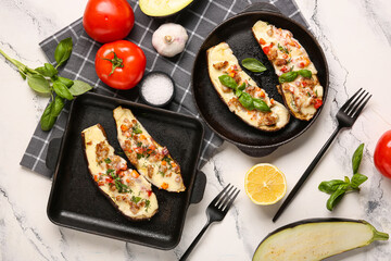 Baking dishes with stuffed eggplants, tomatoes and basil leaves on marble background