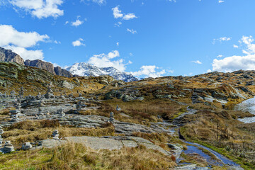 Alpine mountains in autumn, San Bernardino Pass in Switzerland The sky is blue, light, cloudy Many human-built stone pyramids are visible in the foreground