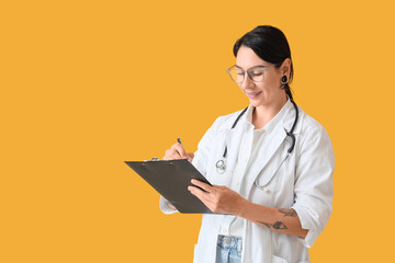 Tattooed female doctor writing in clipboard on yellow background