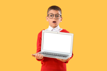 Shocked little schoolboy with blank laptop on yellow background